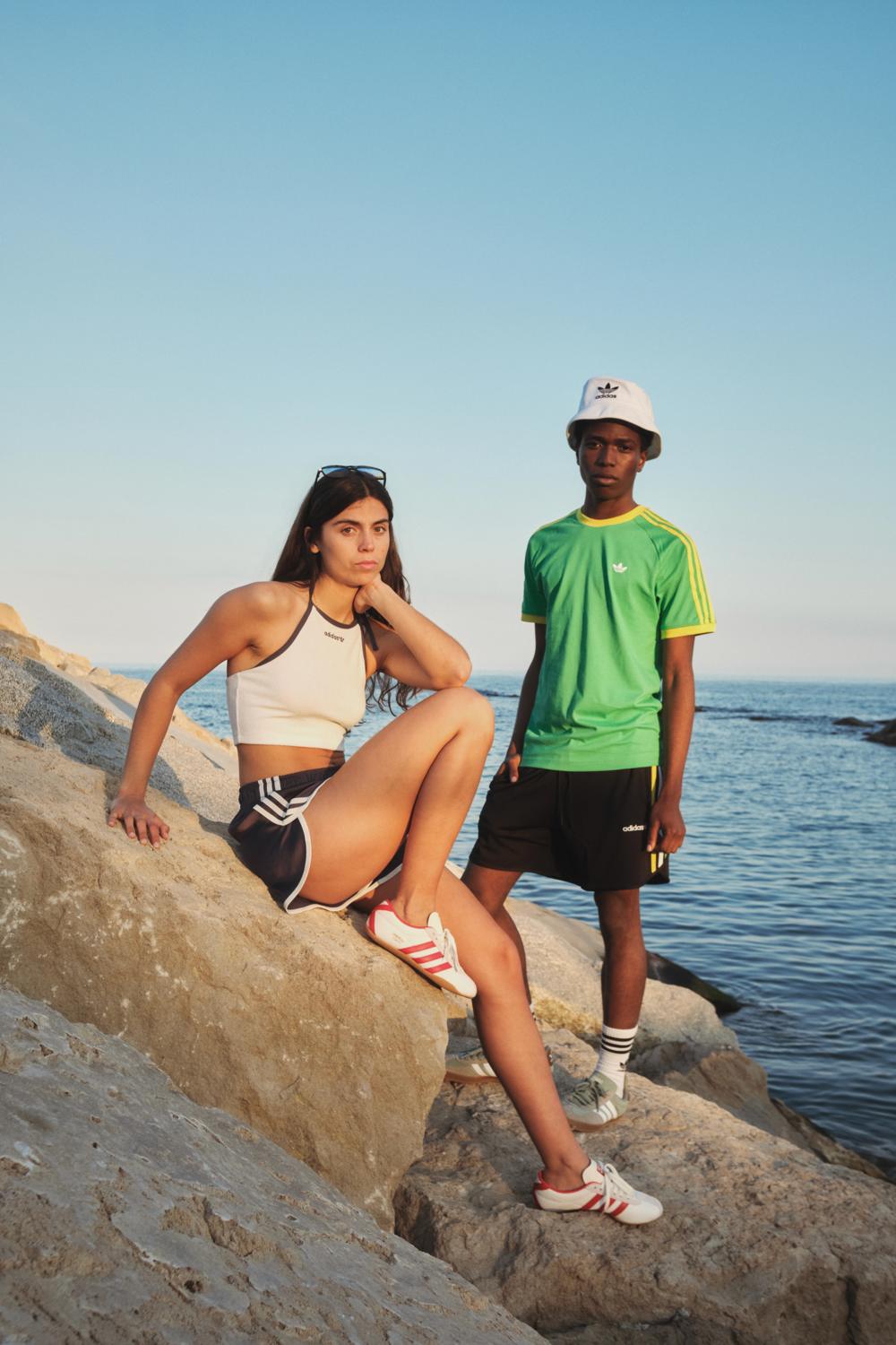 Dos modelos con ropa Adidas sobre unas rocas junto al mar, en formato vertical