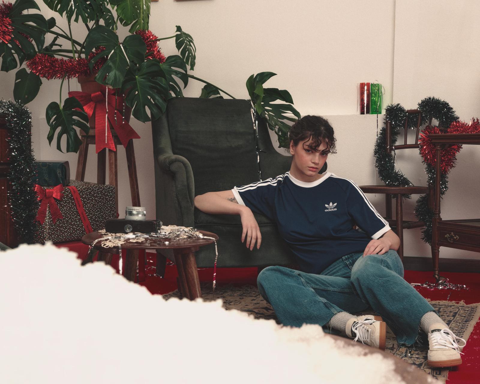 Modelo con camiseta Adidas azul marino sentada en el suelo de un salón con decoración navideña