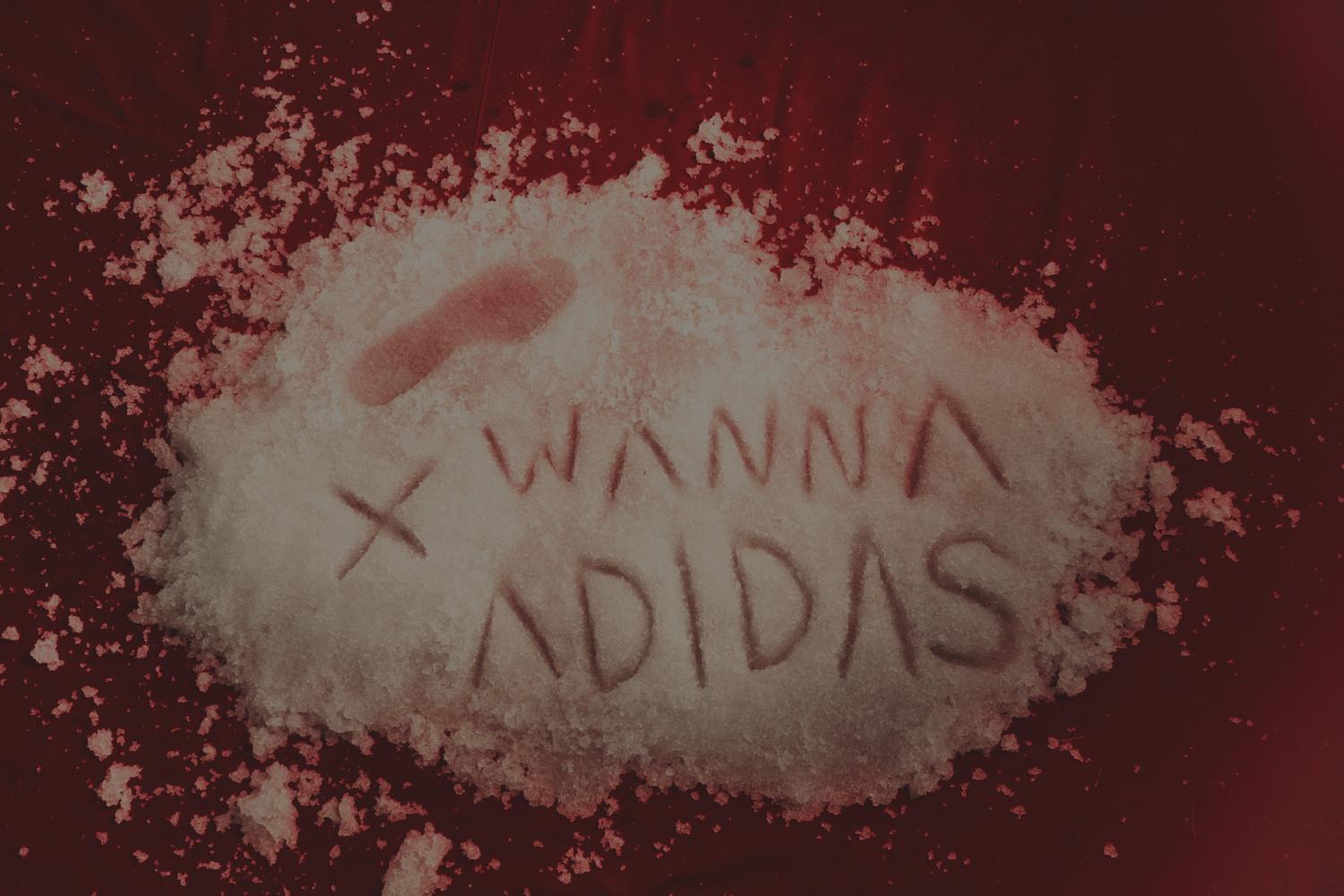 Las palabras «Wanna Adidas» escritas sobre nieve artificial en un fondo rojo