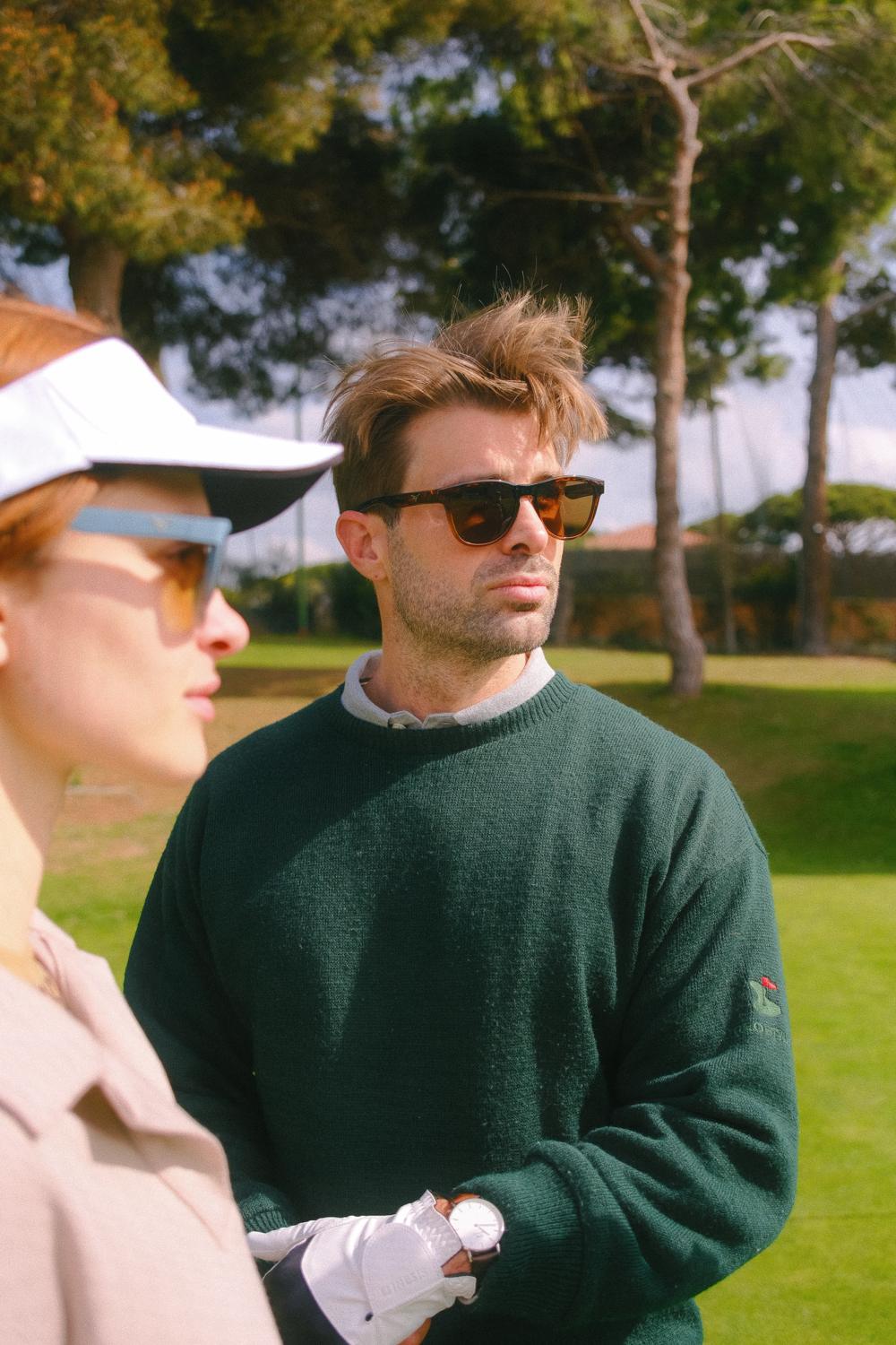 Un hombre con jersey verde y gafas de sol en un campo de golf
