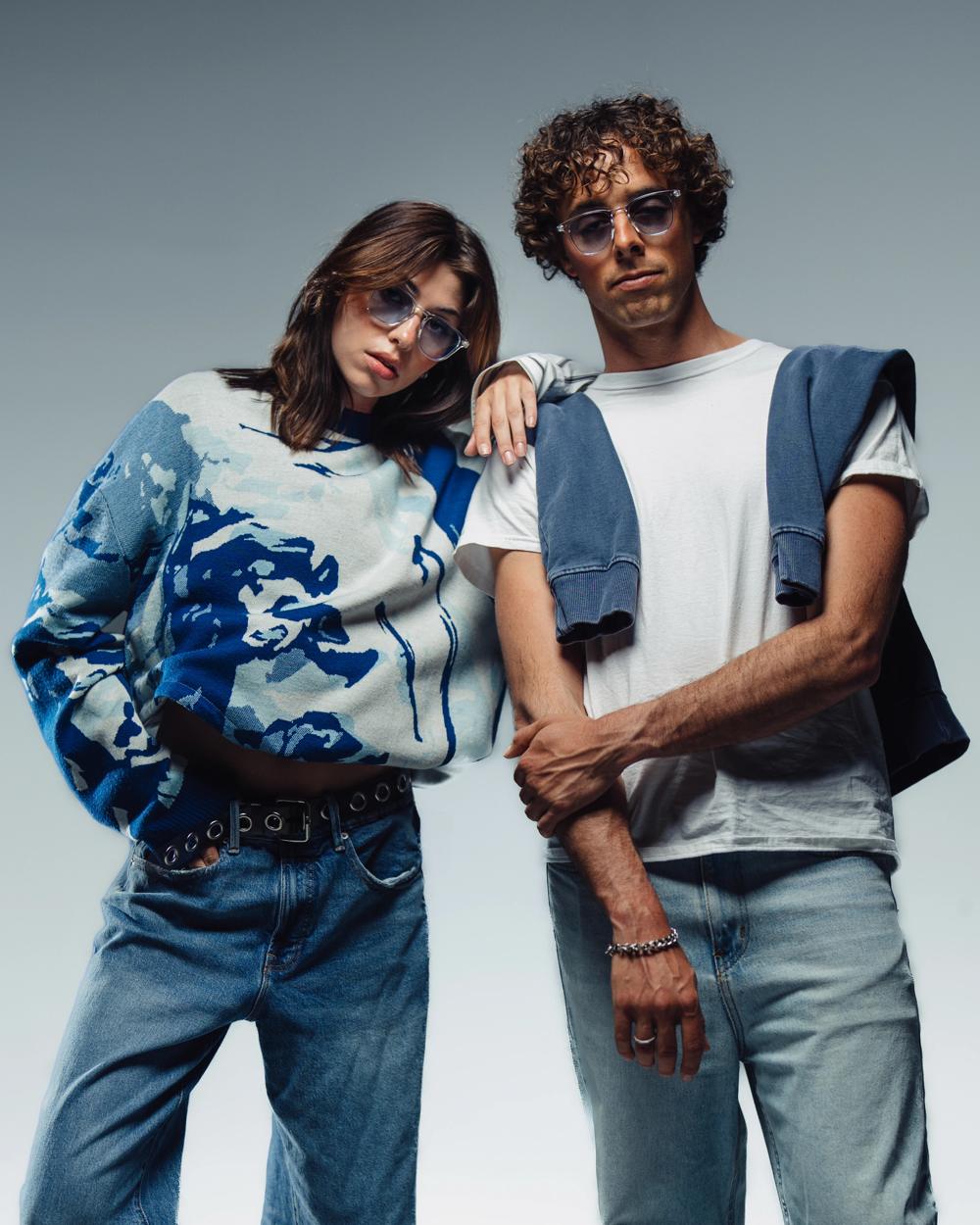 Dos modelos con gafas de sol posan juntos sobre fondo gris